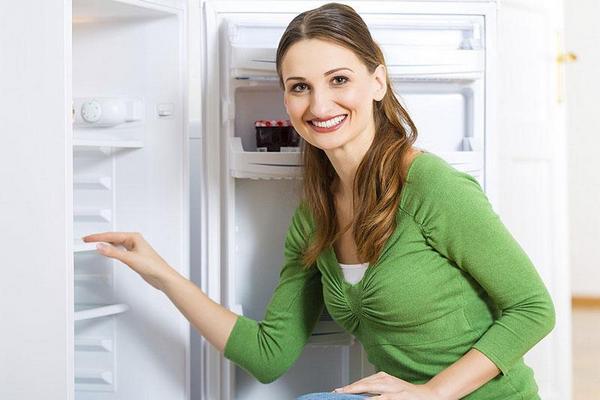  Una niña se para cerca del refrigerador abierto.